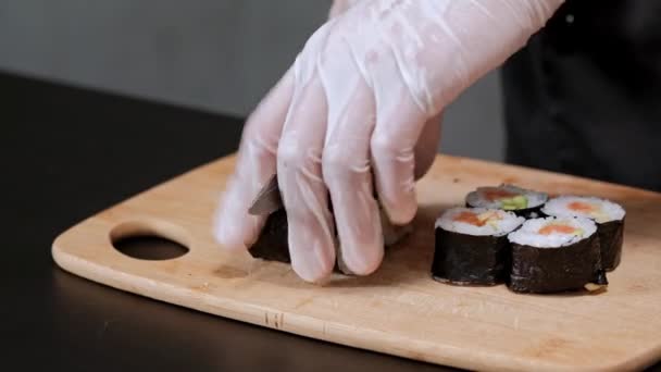 Den unge manliga Sushikocken tillagar japanska sushirullar med ris, lax, avokado och Nori. Restaurangkök, närbild händer. — Stockvideo