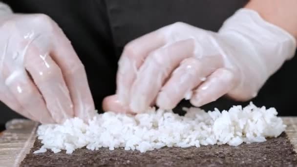 O jovem chef de sushi masculino prepara rolos de sushi japoneses de arroz, salmão, abacate e nori. Restaurante cozinha . — Vídeo de Stock