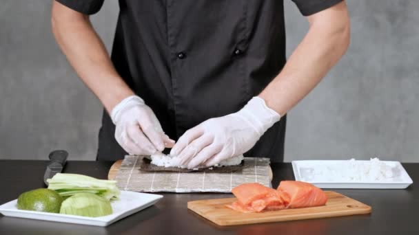 Mladý suši šéfkuchař připravuje japonské Suši z rýže, lososa, avokáda a nori. Restaurace kuchyně. — Stock video