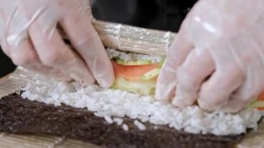 Genç erkek suşi şef pirinç, somon, avokado ve nori Japon suşi rulo hazırlar. Restoran mutfak.