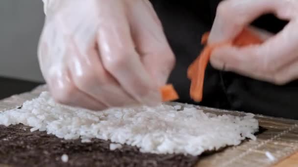 Young male sushi chef prepares Japanese sushi rolls of rice, salmon, avocado and nori. Restaurant kitchen. — Stock Video