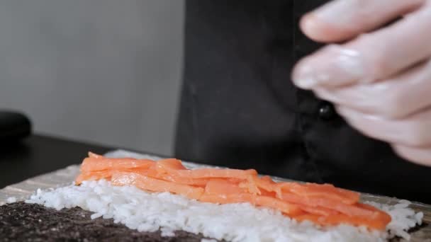 若い男性寿司シェフが、ご飯、サーモン、アボカド、海苔の日本の寿司ロールを用意。レストランキッチン. — ストック動画