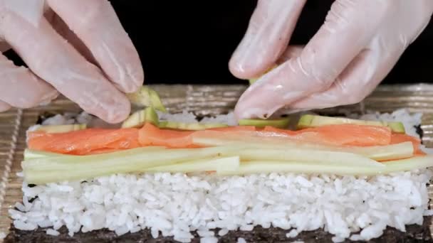 Der junge männliche Sushi-Koch bereitet japanische Sushi-Rollen aus Reis, Lachs, Avocado und Nori zu. Restaurant-Küche. — Stockvideo