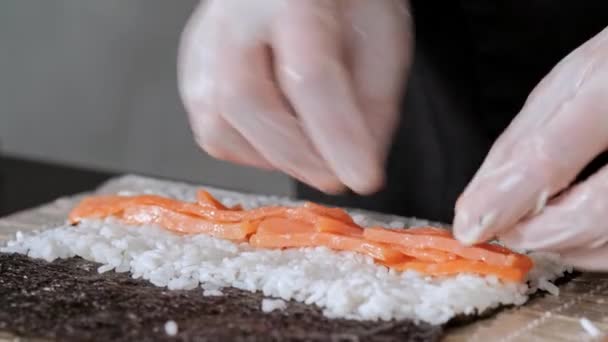 Mladý suši šéfkuchař připravuje japonské Suši z rýže, lososa, avokáda a nori. Restaurace kuchyně. — Stock video