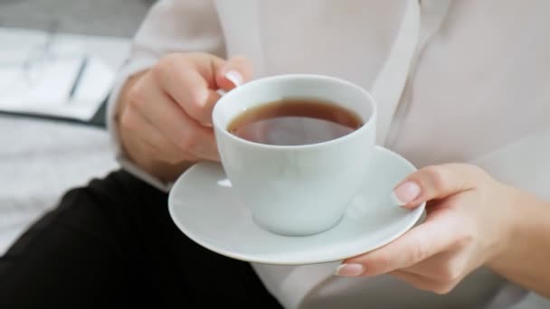 Una giovane bella donna bionda con i capelli corti con bicchieri beve caffè da una tazza bianca in un appartamento leggero . — Video Stock