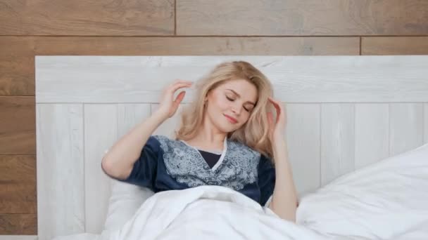 Joven hermosa mujer rubia en albornoz acostada en la cama sobre una almohada blanca . — Vídeos de Stock