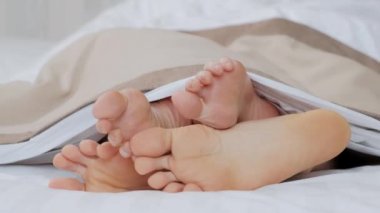 İki çift bacak, bir erkek ve bir kadın yatağın üzerinde beyaz bir battaniyenin altında..