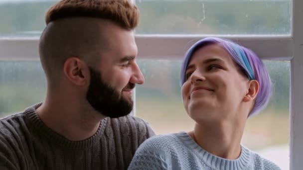 Jeune beau couple en chandails serrant à la maison par la fenêtre. Coupes de cheveux courtes . — Video