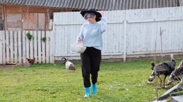 Молода красива жінка-фермер в светрі і чорний капелюх з краєм на тлі зеленої трави і притулку. Тримає курячі яйця . — стокове відео