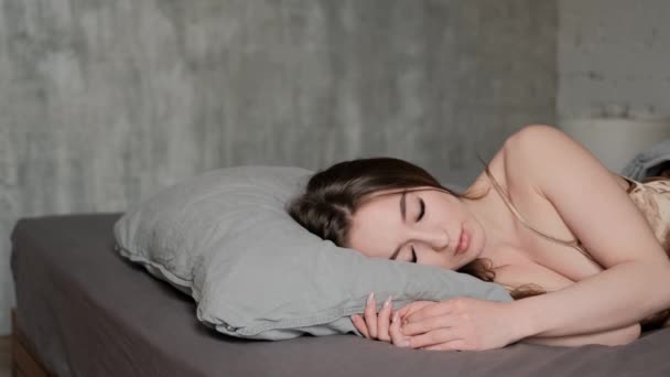 Eine junge schöne brünette Frau liegt auf dem Bett, schläft, dreht sich im Schlaf um, streckt sich. — Stockvideo