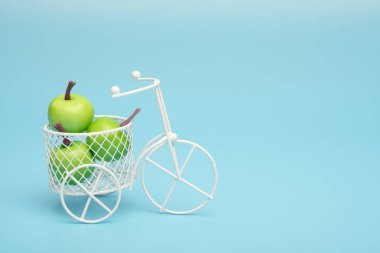 Mini meyve ile dolu bir sepet ile beyaz tel bisiklet. Sebze ve meyve ile kova yakın. Mavi arka plan. Hasat ve meyve ve sebze teslim kavramı.