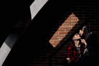 Evin bir tuğla duvara karşı ekose gömlek genç güzel çift. Pencereden gelen ışık gölgeler oluşturur.