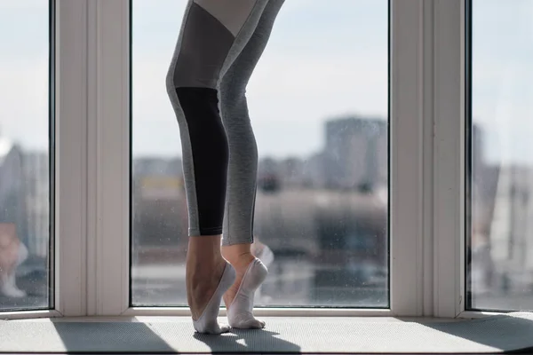 Close-up de pernas femininas em sportswear e meias. Treinamento de movimentos de dança e alongamento na varanda contra a janela . — Fotografia de Stock