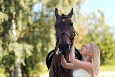Genç ve çekici sarışın bir kadın kahverengi bir ata sarılıyor..