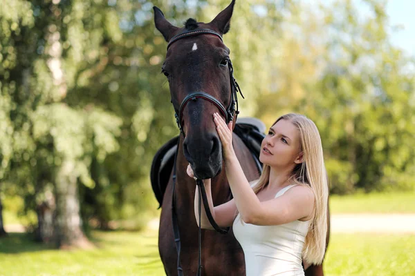 Joven mujer rubia atractiva abraza a un caballo marrón . — Foto de Stock