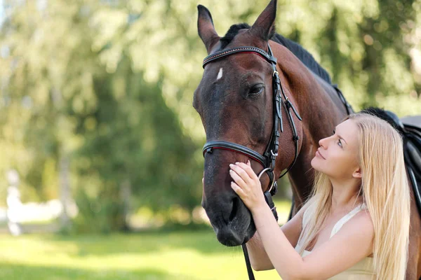 Joven mujer rubia atractiva abraza a un caballo marrón . — Foto de Stock