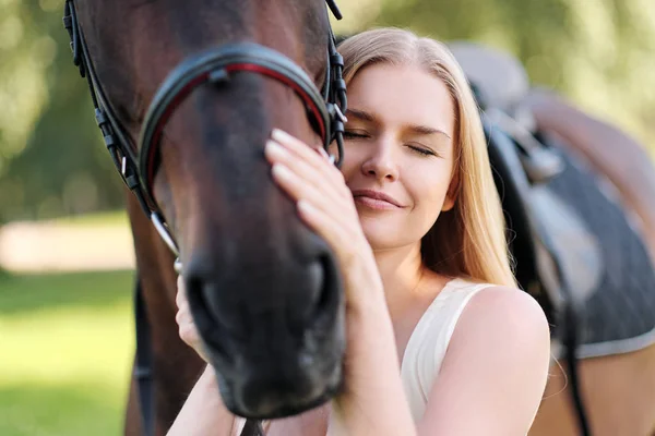 Young attractive blond woman hugs a brown horse. — Stock Photo, Image