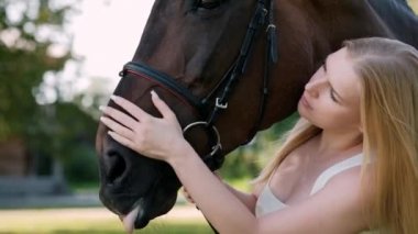 Genç ve çekici sarışın bir kadın kahverengi bir ata sarılıyor..