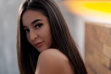 Çıplak omuzları yatakta yatan kahverengi gözlü güzel esmer kız. Yakından yüzleşin. Asya ve Doğu tipi görünüm.