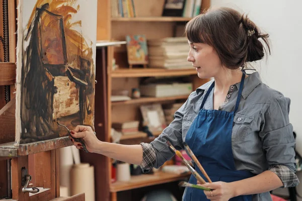 Ung vacker kvinna målare bland stafvlar och dukar i en ljus Studio. — Stockfoto