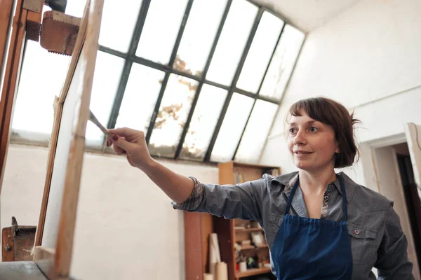 Joven mujer hermosa pintor entre caballetes y lienzos en un estudio brillante . — Foto de Stock