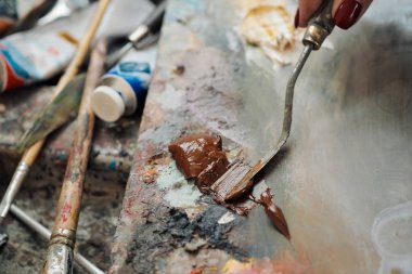 Kadın sanatçı bir palet bıçağı çizer. Paletüzerinde farklı renklerde yağlı boyalar.