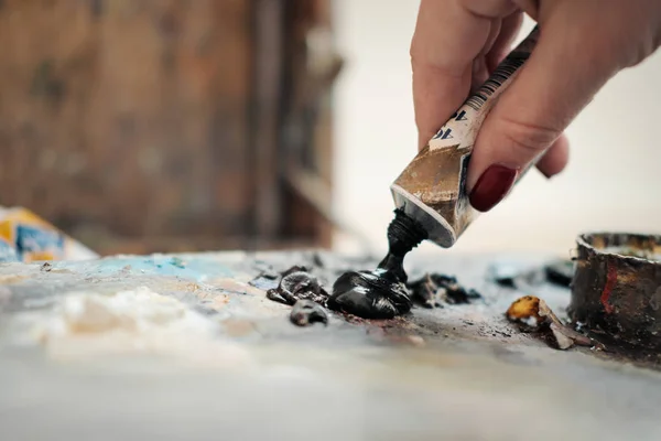 Una artista presiona pintura al óleo sobre una paleta de un tubo . —  Fotos de Stock