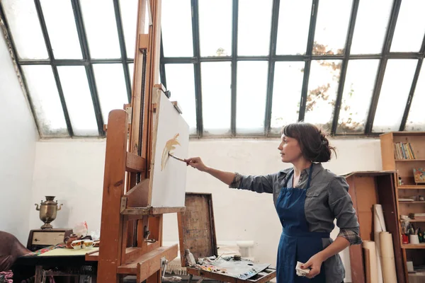 Jeune belle femme peintre parmi les chevalets et toiles dans un studio lumineux . — Photo