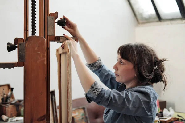 Mujer artista sujeta un lienzo en un gran caballete de madera . — Foto de Stock