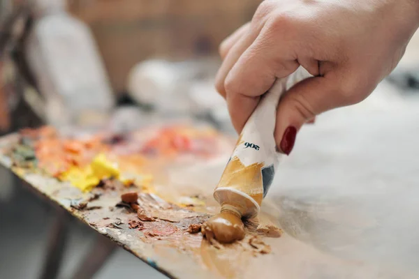 Una artista presiona pintura al óleo sobre una paleta de un tubo . — Foto de Stock