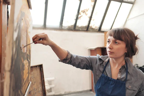 Mujer artista pinta un cuadro sobre lienzo. Luminoso estudio de arte con una gran ventana. caballetes y lienzos . — Foto de Stock