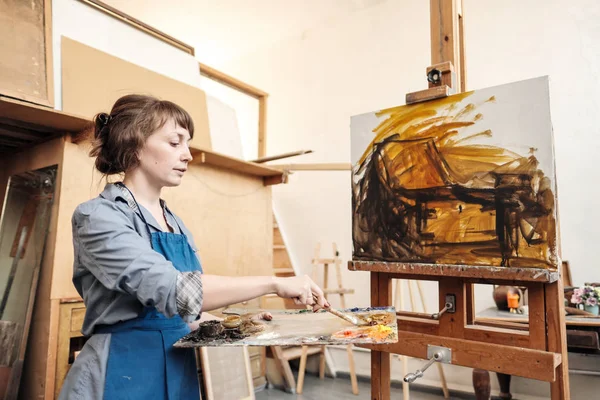 Joven mujer hermosa pintor entre caballetes y lienzos en un estudio brillante . — Foto de Stock