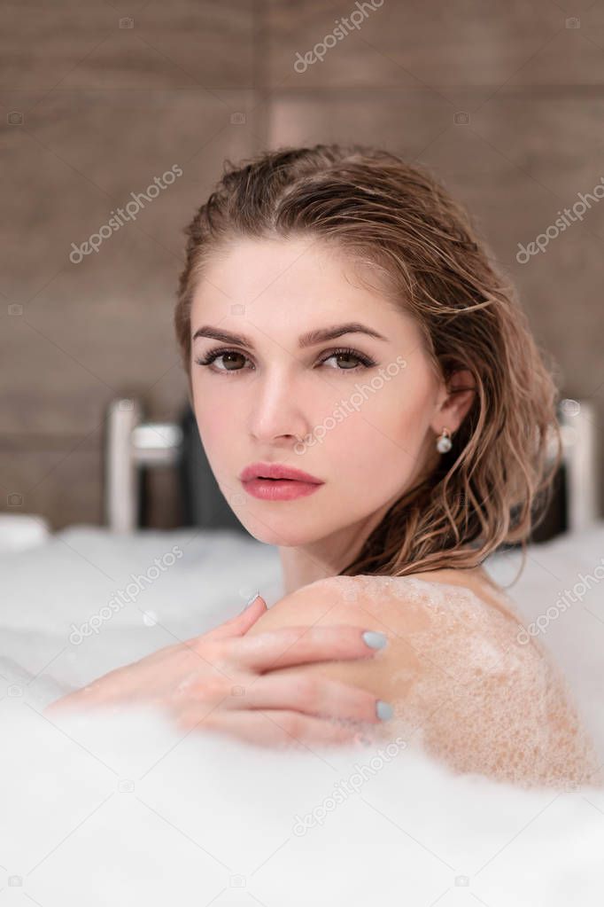 Attractive blonde woman lying in bathtub in foam in hotel.