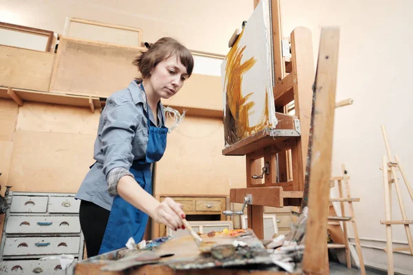 Ung vacker kvinna målare bland stafvlar och dukar i en ljus Studio. — Stockfoto
