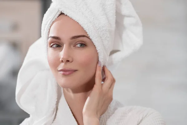 Kafasından beyaz havlu ile çekici orta yaşlı sarışın kadın ve ayna banyoda ayakta bornoz. O cilde dokunur ve gülümsüyor.