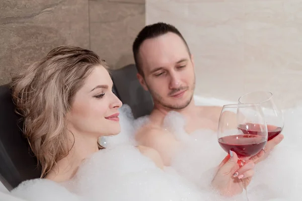 一对迷人的夫妇,一个男人和一个女人,一对夫妻,躺在泡泡浴里,喝着红酒. — 图库照片