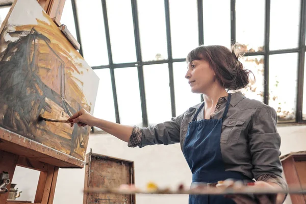 Женщина-художник рисует картину на холсте. Светлая художественная студия с большим окном. Удобства и холсты . — стоковое фото