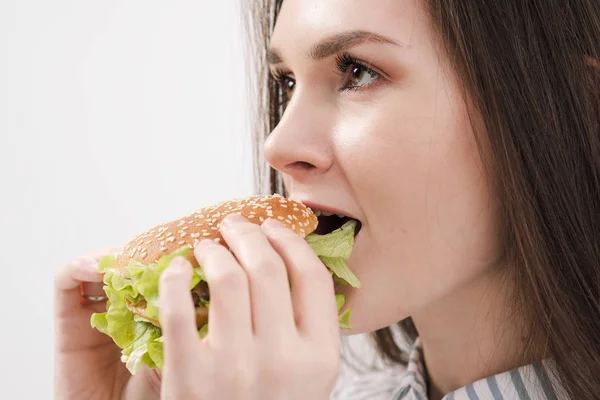 Jeune belle fille brune sur fond blanc avec un hamburger dans les mains. Manger avec plaisir fast food . — Photo