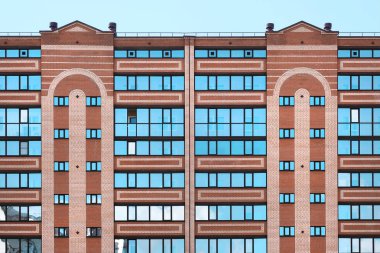 Çok katlı modern ev yakın çekim. Tuğla, pencereler, camdaki gökyüzünün yansımaları. Gündüz, güneş.