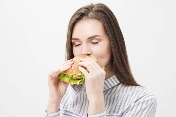 Jeune belle fille brune sur un fond blanc avec un hamburger dans ses mains . — Photo