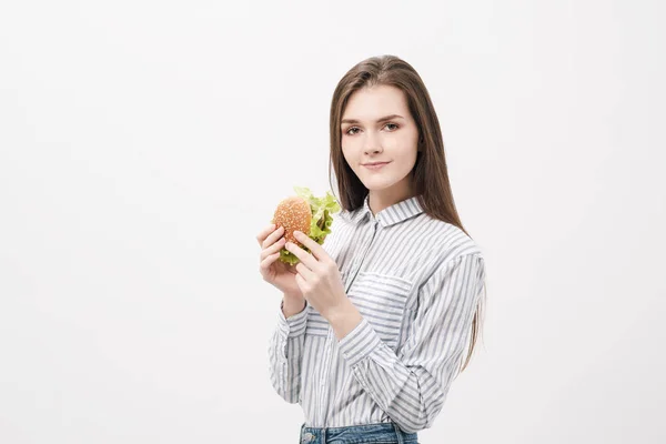 Молодая красивая брюнетка на белом фоне с гамбургером в руках . — стоковое фото