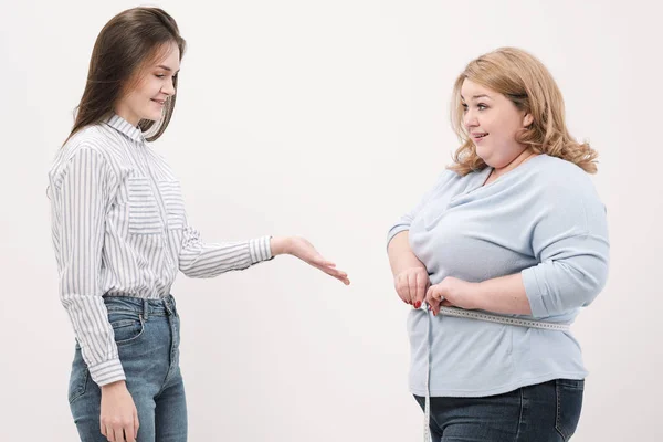 Een dikke vrouw meet haar taille met een meetlint in Casual kleding op een witte achtergrond. — Stockfoto