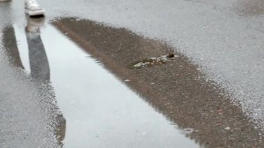 Kotlu ve spor ayakkabılı kadın bacaklarına yakın çekim. Yağmurlu bir günde su birikintilerinde yürüyorum.