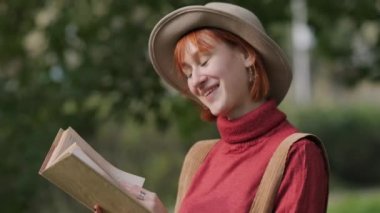 Şapkalı, kazaklı, doğal bir parkta kitap okuyan çekici bir kadın. Sonbahar serin günü.