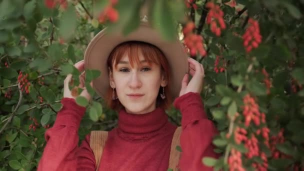 모자를 쓰고 짧은 머리를 하고 가을에 자연 공원에서 테라코타 스웨터를 입은 매력적 인 빨간 머리 소녀. — 비디오