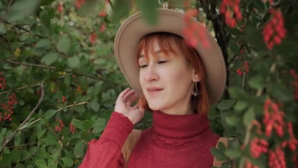 秋天的一天，年轻迷人的红头发姑娘，头戴一顶帽子，穿着一件兵马俑毛衣，站在一个自然公园里. — 图库视频影像