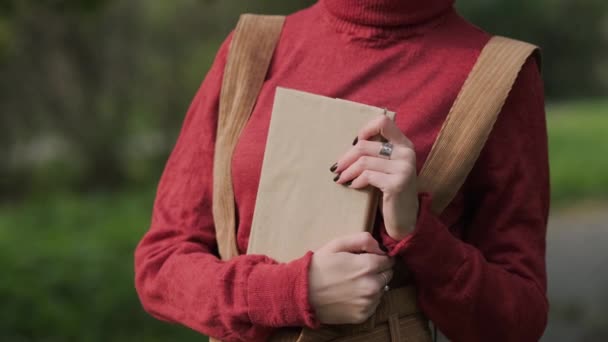 Junge attraktive rothaarige Frau mit Hut und Pullover, die auf einer Bank in einem Naturpark ein Buch liest. Herbstlicher kühler Tag. — Stockvideo