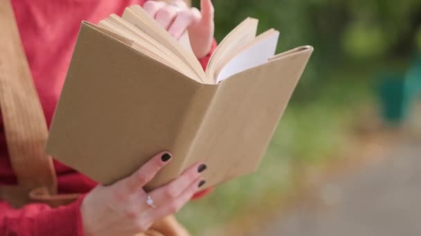 Jovem mulher ruiva atraente em um chapéu e suéter lendo um livro em um banco em um parque natural. Outono dia fresco . — Vídeo de Stock