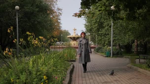 Giovane ragazza dai capelli corti rossa attraente in un berretto nero e cappotto grigio in un parco naturale in una giornata d'autunno . — Video Stock