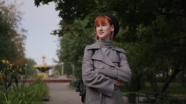 Young attractive redhead short-haired girl in a black beret and gray coat in a natural park on an autumn day. — Stock Video